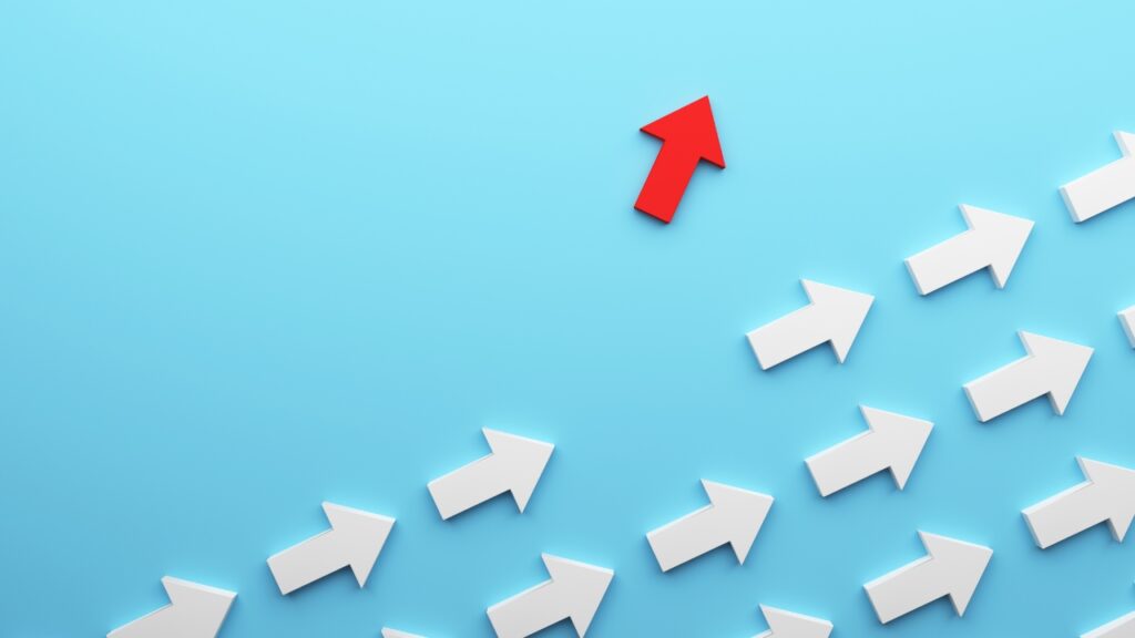 A group of white arrows pointing upward, with one red arrow breaking away in a different upward direction—symbolizing executive leadership development.